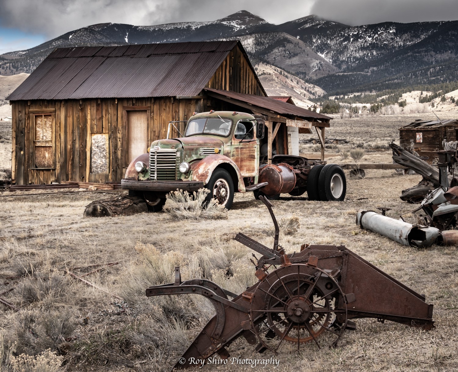 Rustic truck in front of a rustic cabin with a mountain range in the background